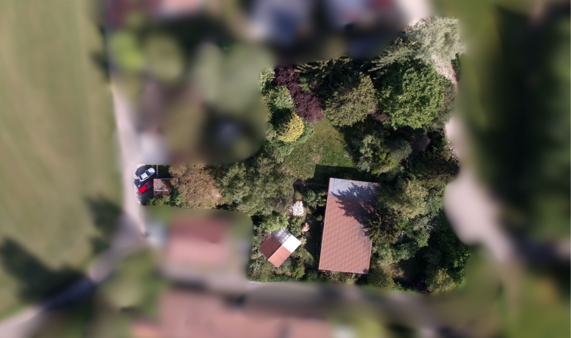 Luftaufnahme eines Hauses mit Garten, umgeben von Bäumen, ein Auto am Straßenrand.