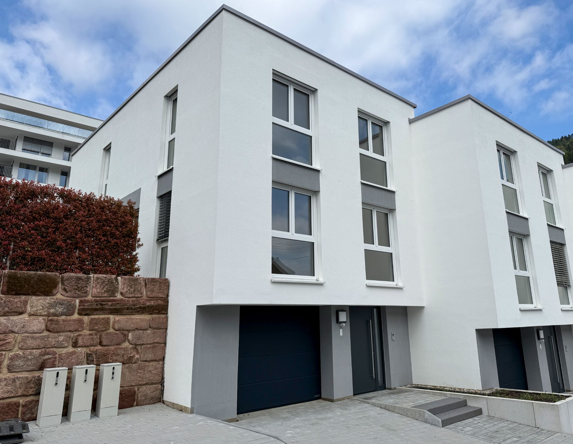 Moderne weiße Doppelhaushälfte mit Garage, drei Etagen und großen Fenstern.