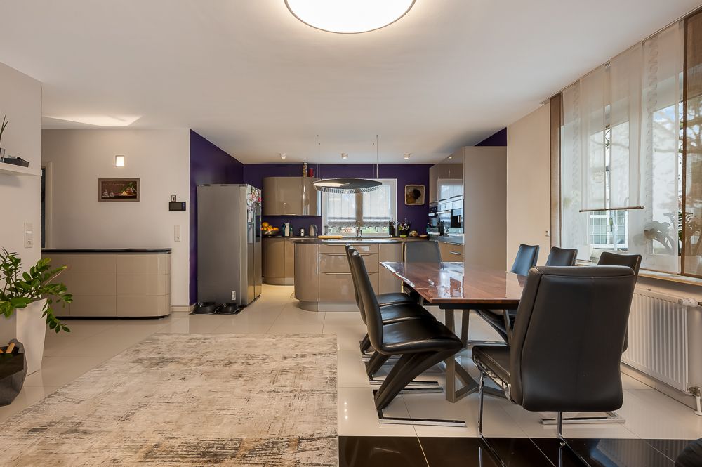 Moderne offene Küche mit Essbereich, großem Holztisch und sechs schwarzen Stühlen, viel Tageslicht.