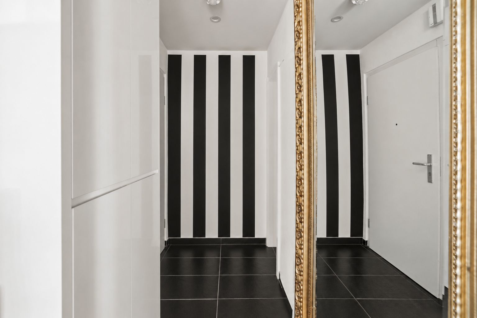 Flur mit schwarz-weiß gestreifter Wand, weißen Türen und großem Spiegel.