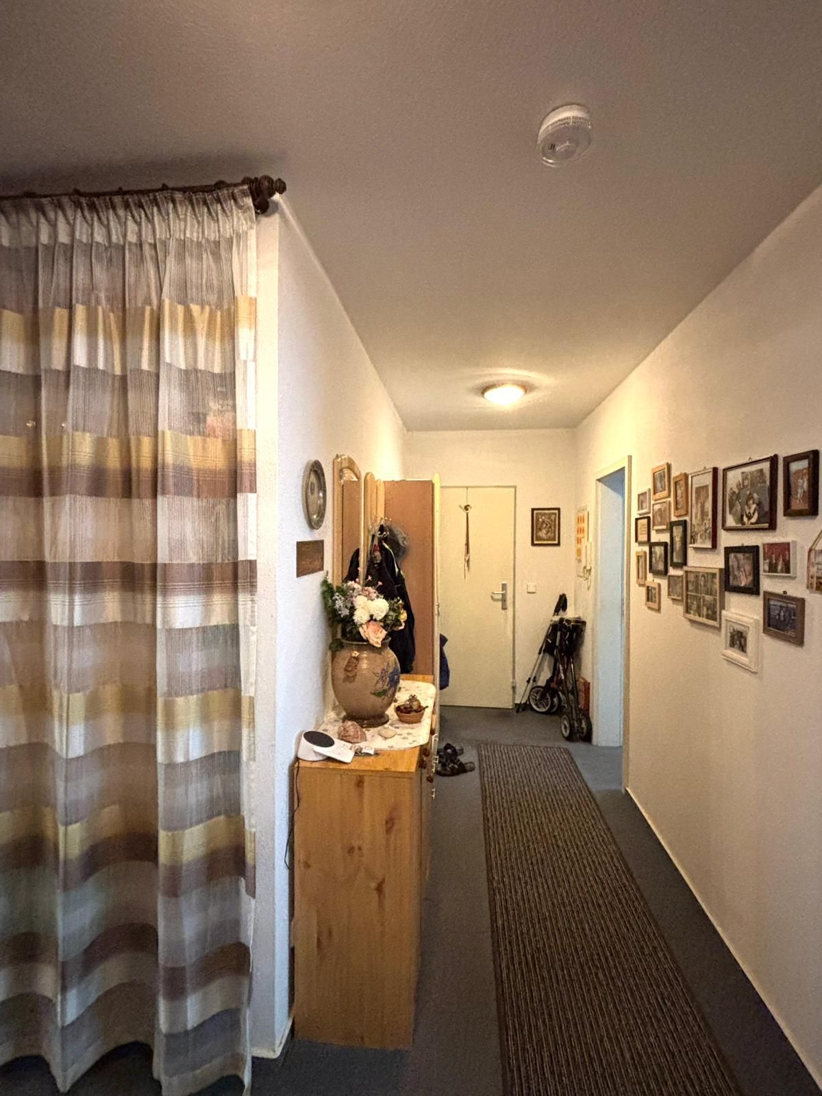Flur mit Teppichläufer, Kommode, Garderobe, Vorhang und vielen Bildern an der Wand.