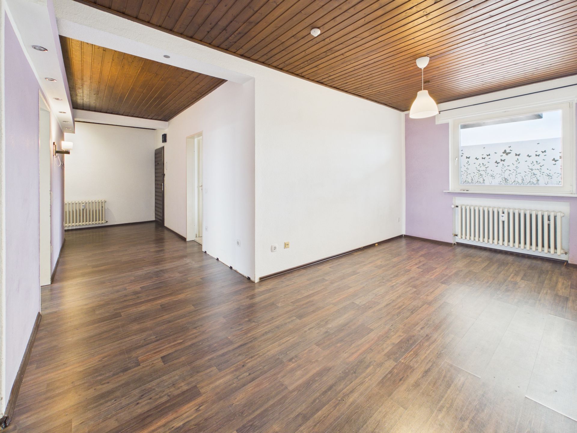 Leerer Raum mit Holzdecke, Holzboden, Fenster und Heizkörper.