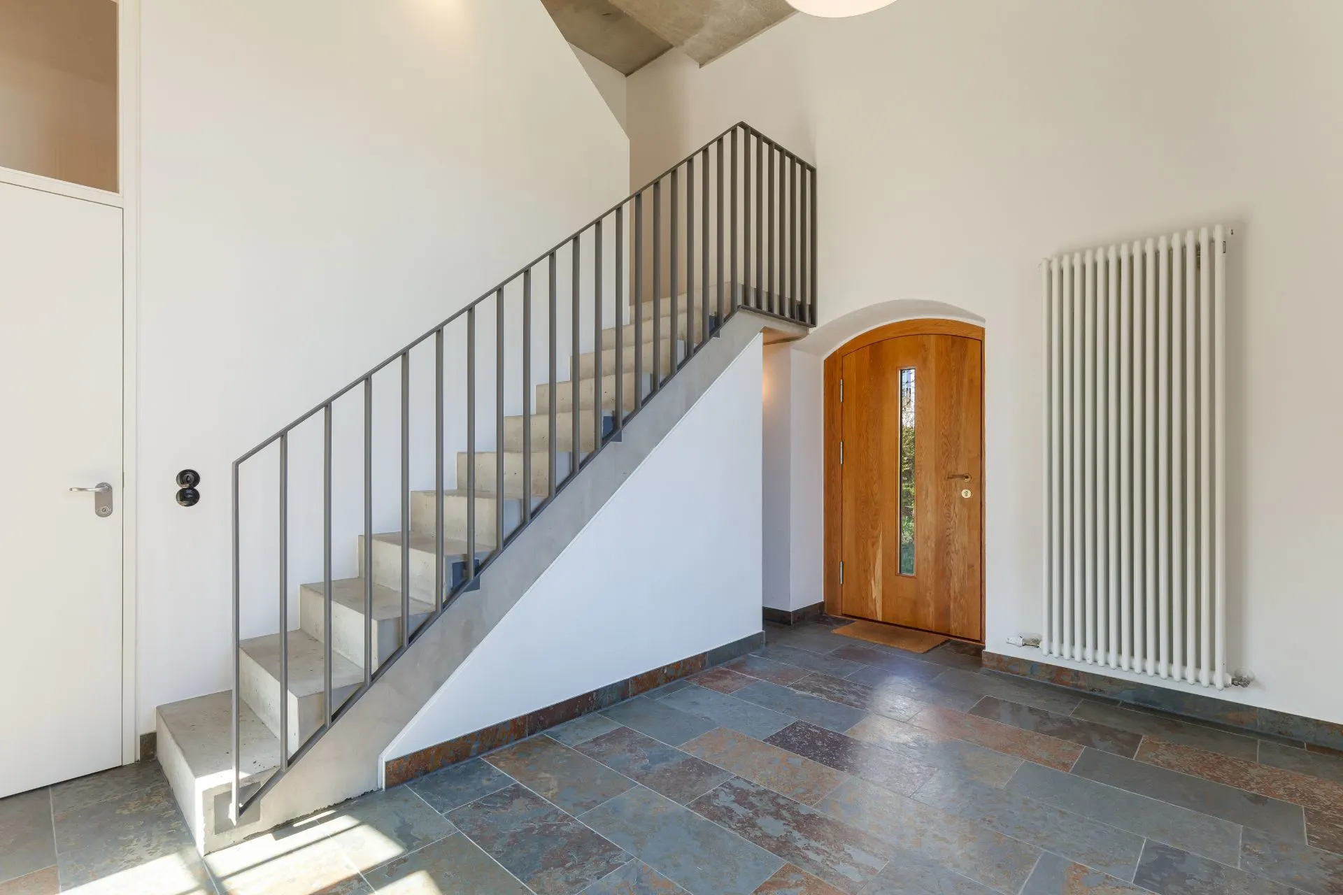 Heller Flur mit Steintreppe, Holztür und Heizkörper an der Wand.