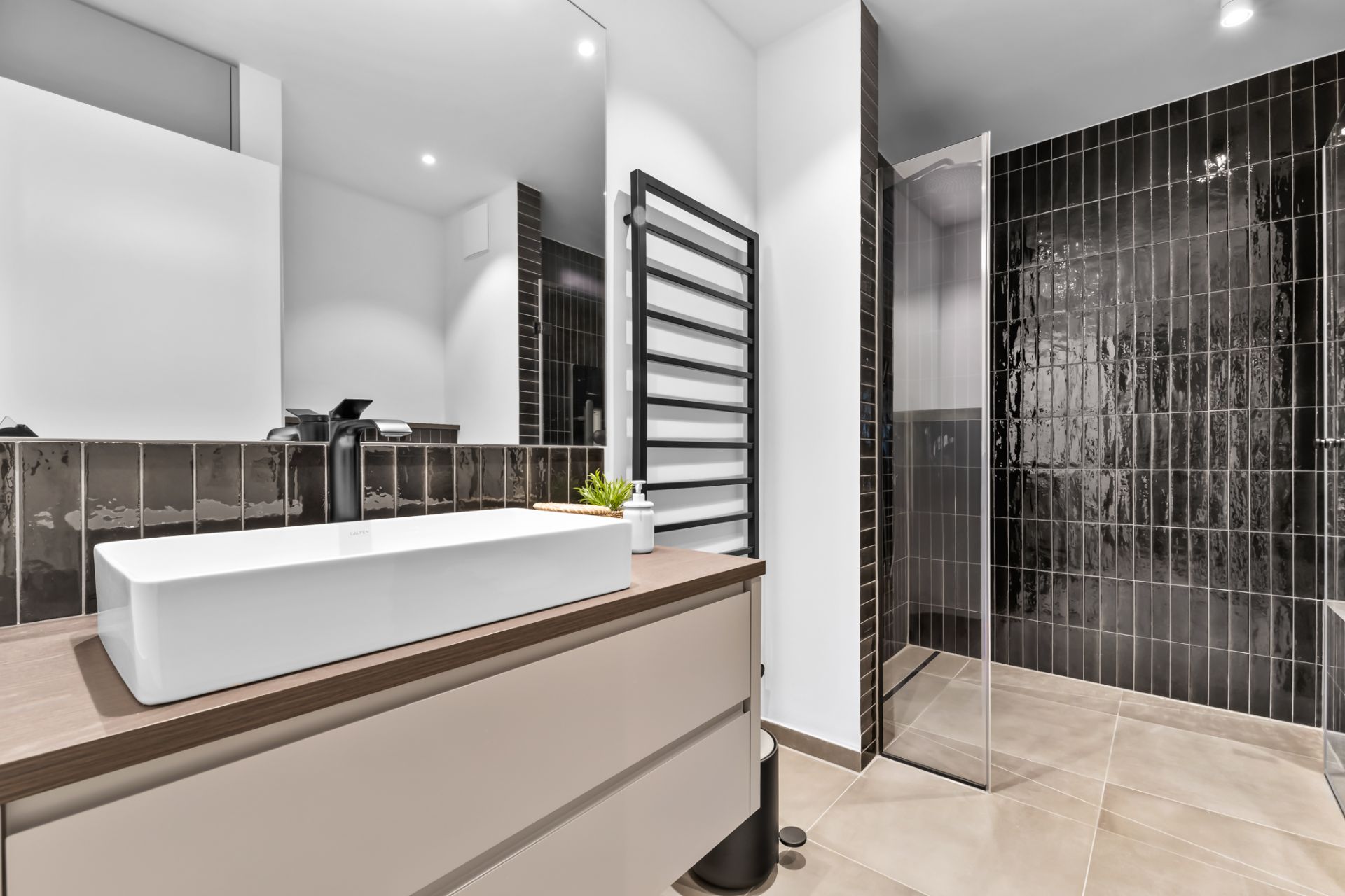 Modernes Badezimmer mit großem Waschbecken, Spiegel und bodentiefer Dusche mit dunklen Fliesen.