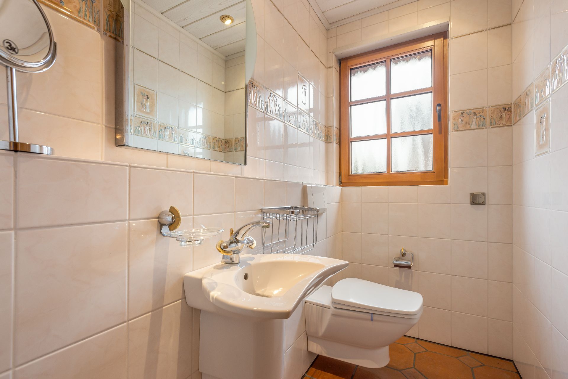 Kleines Badezimmer mit Wand-WC, Waschbecken, Spiegel und Fenster mit Holzrahmen.