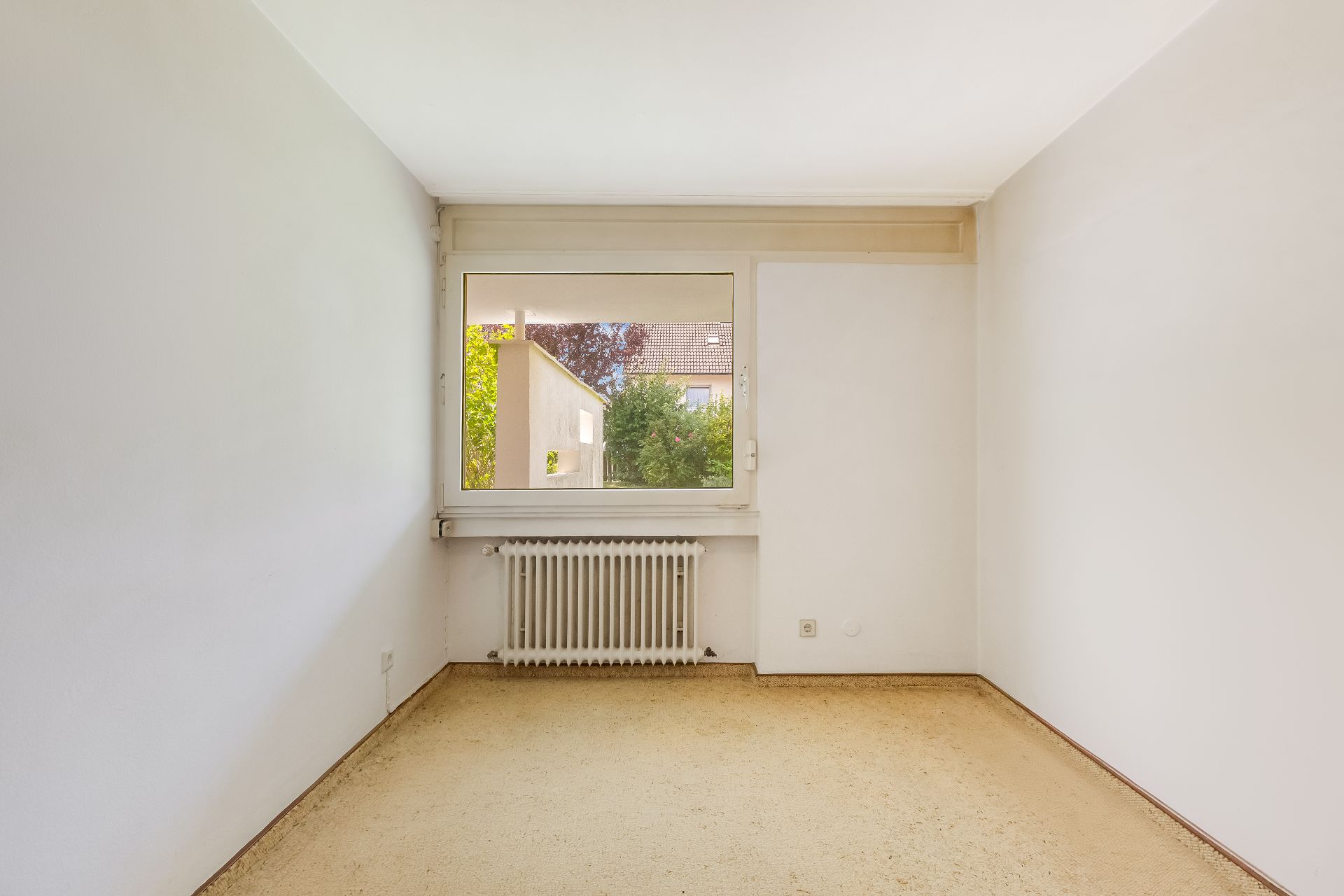 Leerer Raum mit weiß gestrichenen Wänden, Fenster und Heizkörper unter dem Fenster.