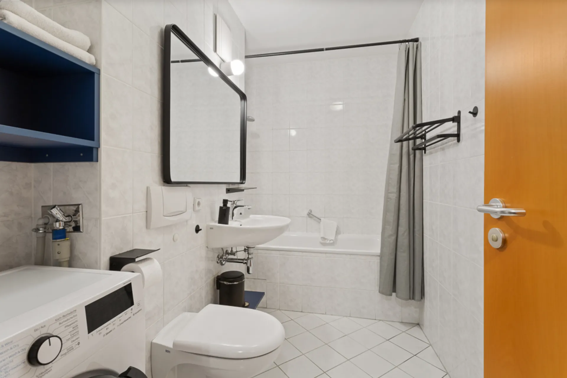 Modernes Badezimmer mit Badewanne, Waschbecken, WC, Spiegel, Waschmaschine und Handtüchern.