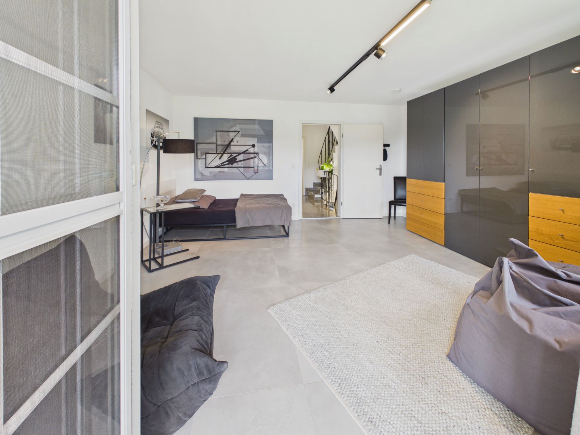 Modernes Schlafzimmer mit grauen Möbeln, einem Bett, Kleiderschrank und Sitzsäcken auf einem hellen Teppich.