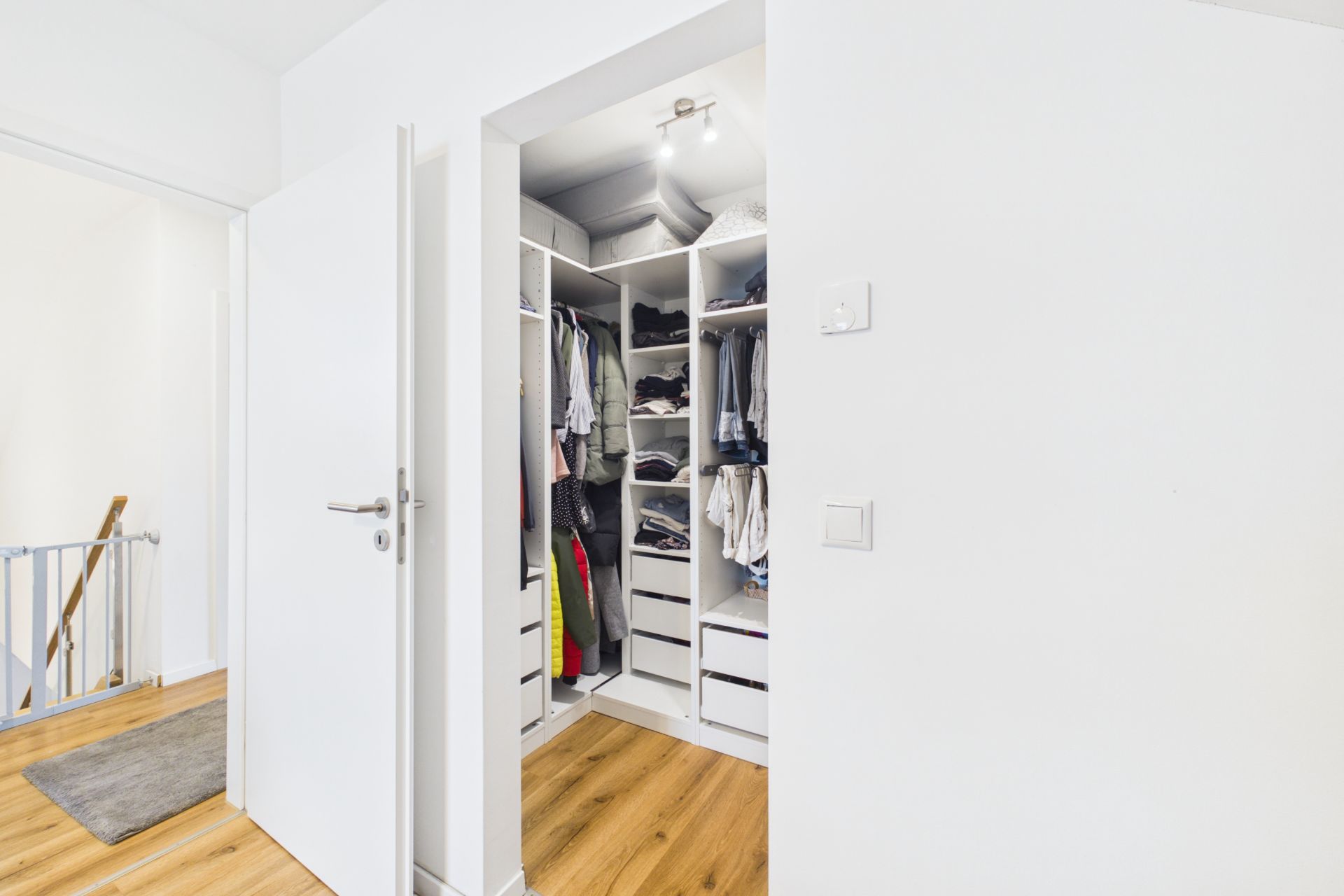 Begehbarer Kleiderschrank mit offenen Regalen und hängender Kleidung, heller Holzboden.