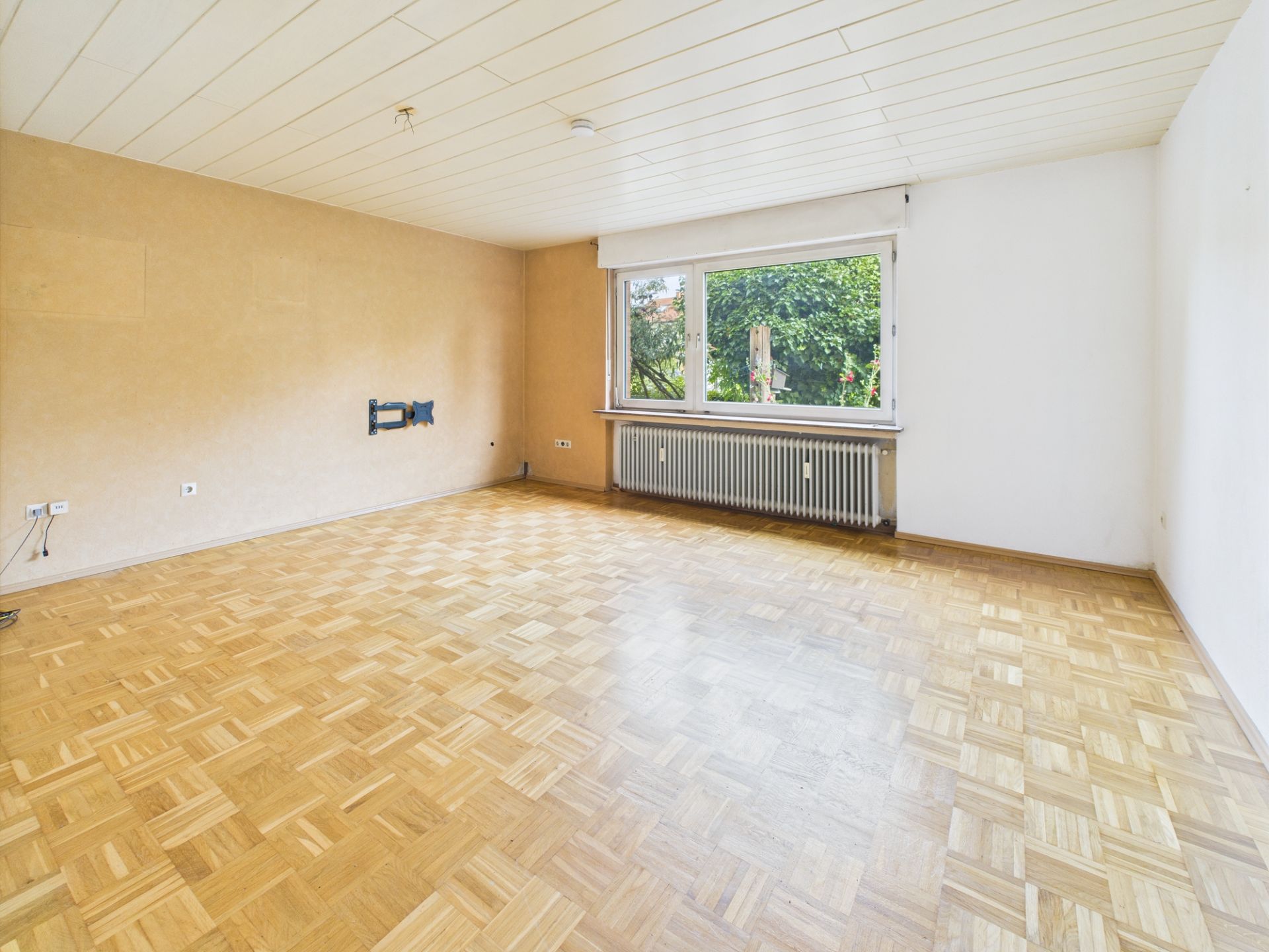 Leerer Raum mit Parkettboden, großem Fenster und Heizkörper unter dem Fenster.