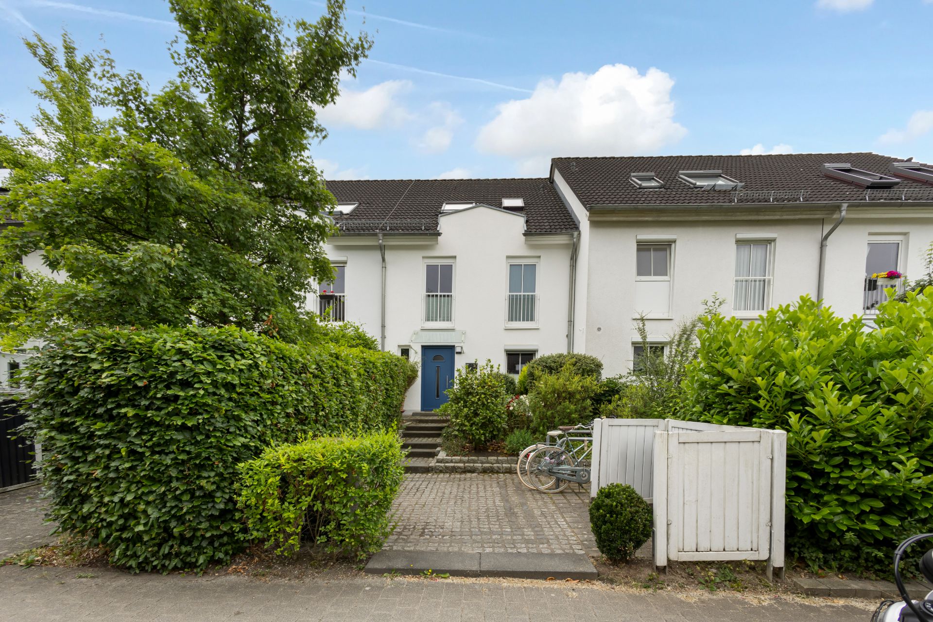 Reihenhaus mit weißer Fassade, blauem Eingang und Vorgarten mit Fahrrädern.