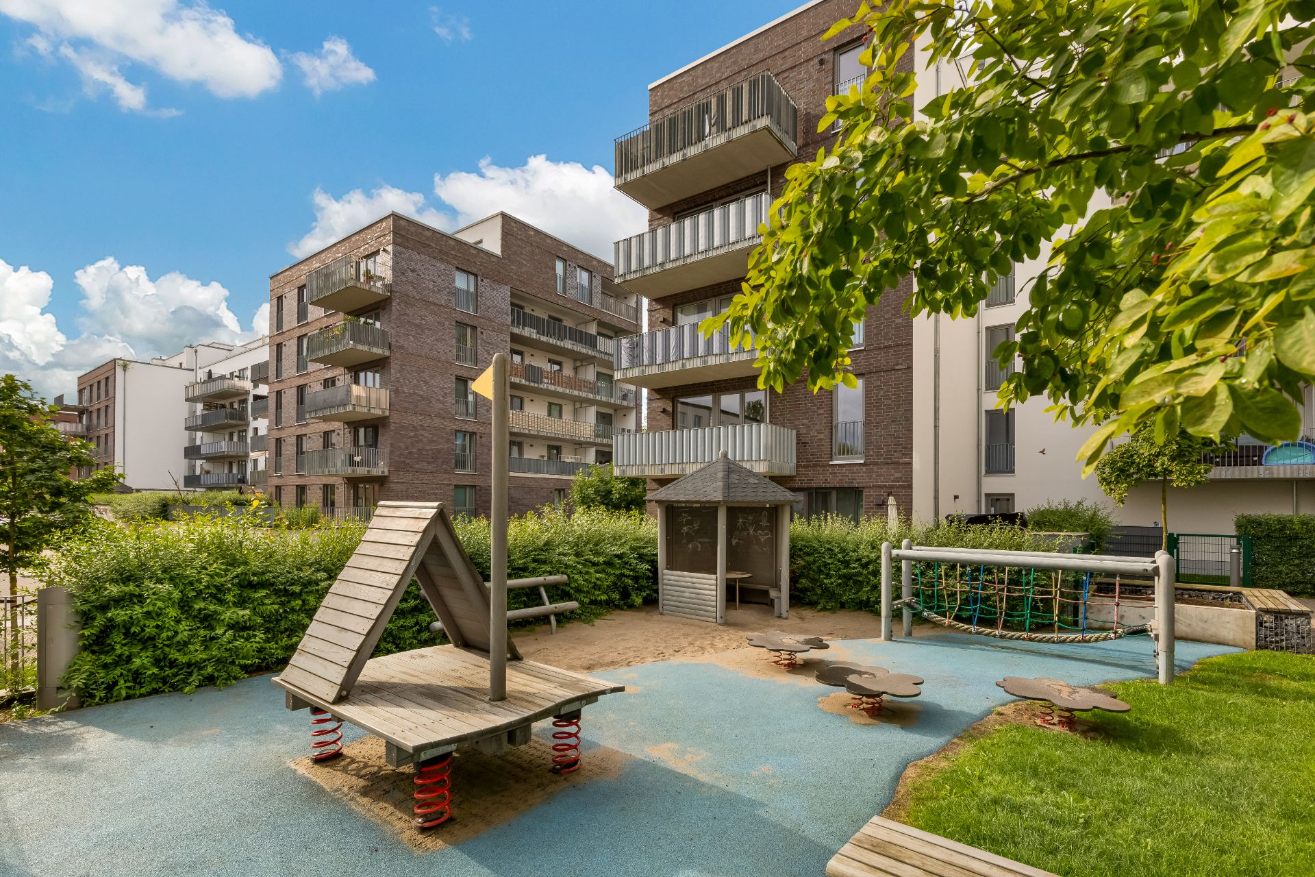 Moderner Wohnkomplex mit Spielplatz, Klettergerüst und Sitzbereich im Freien.