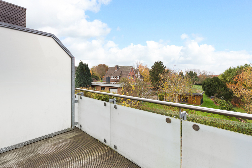 Balkon mit Glasgeländer und Blick auf Gärten und ein Wohnhaus im Hintergrund.