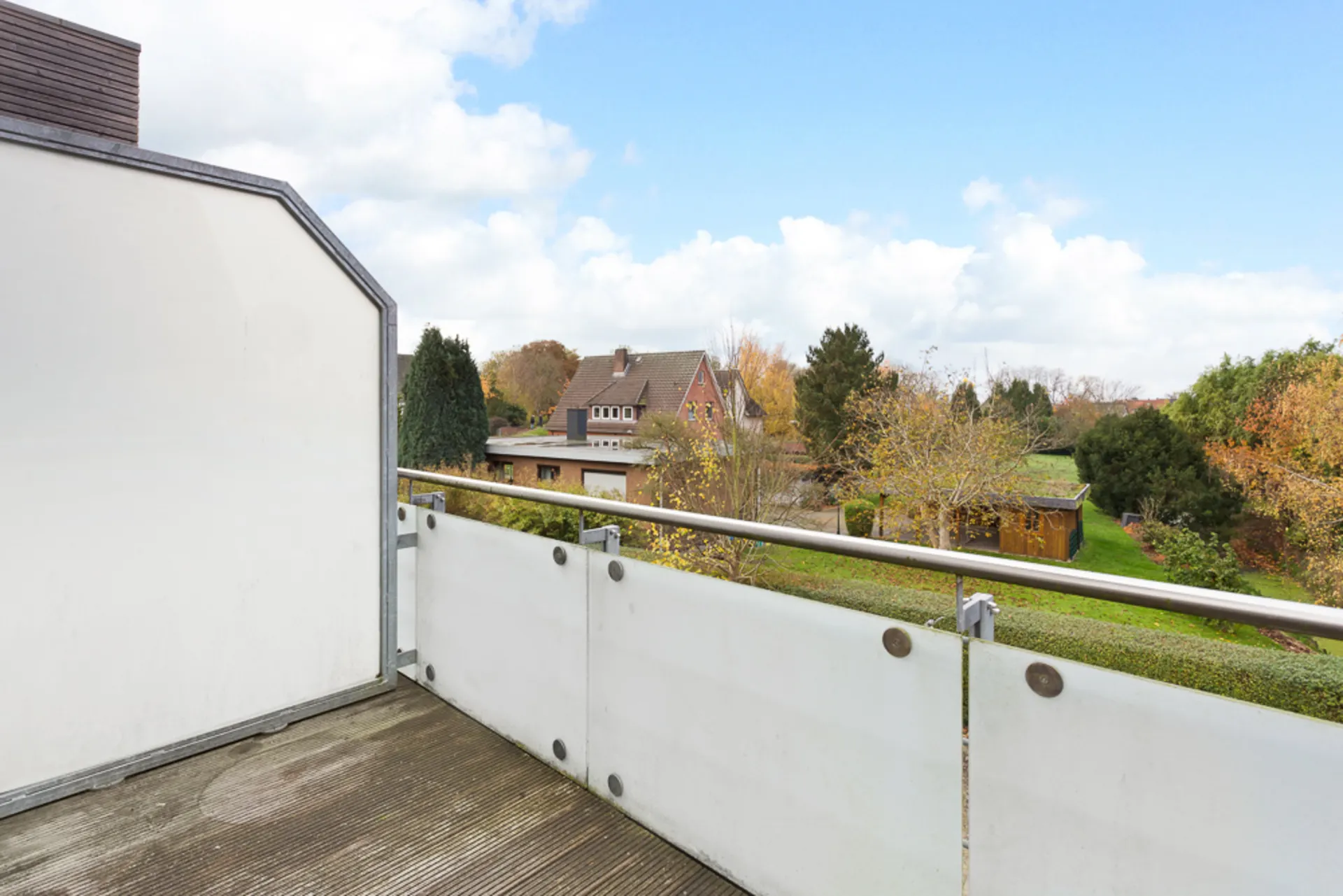 Balkon mit Glasgeländer und Blick auf Gärten und ein Wohnhaus im Hintergrund.
