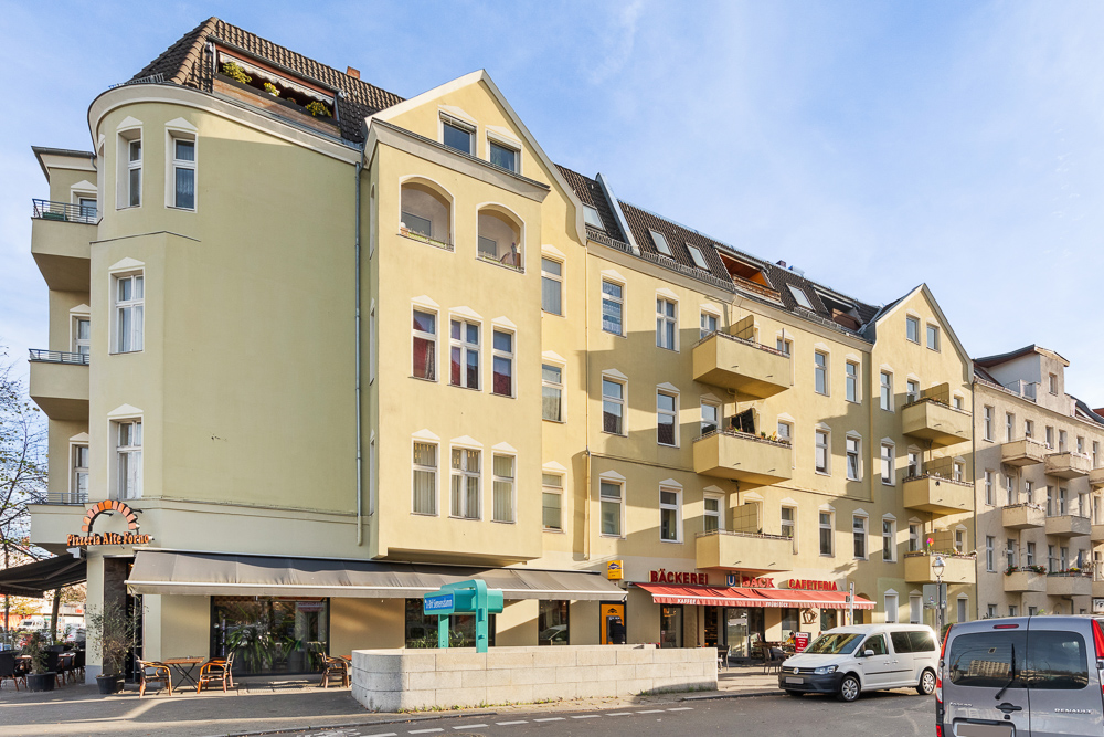 Mehrstöckiges Wohnhaus mit Balkonen, Geschäften und Cafés im Erdgeschoss.