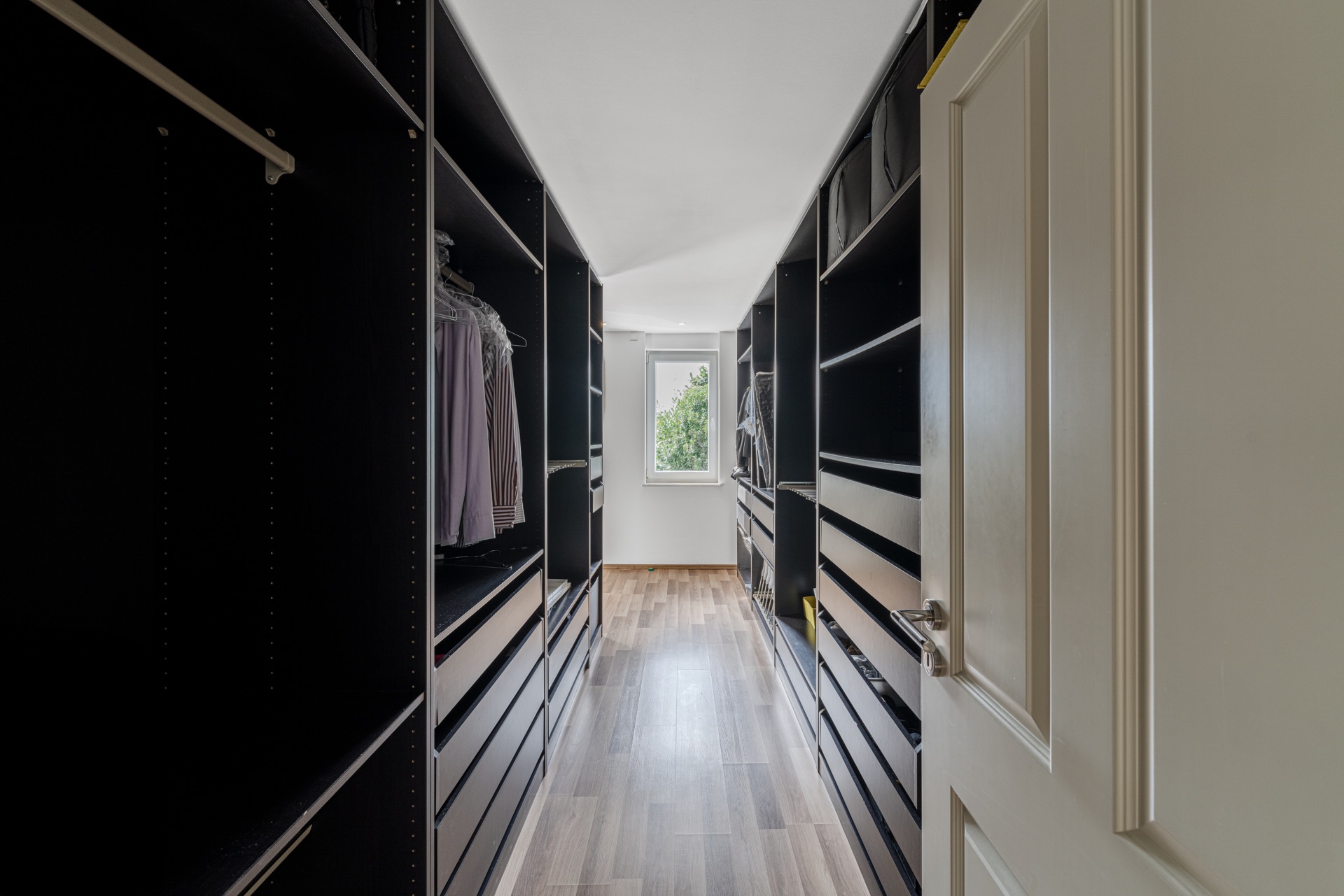 Begehbarer Kleiderschrank mit offenen Regalen und Kleiderstangen, am Ende ein Fenster.