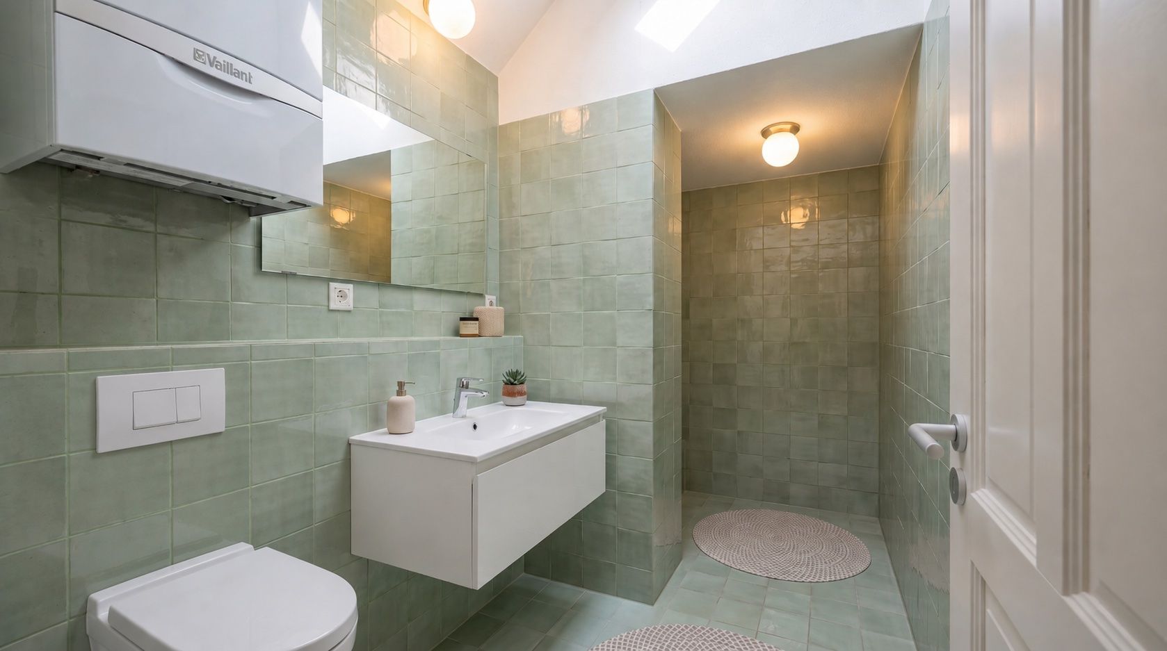 Modernes Badezimmer mit grünen Fliesen, Waschbecken, Toilette und begehbarer Dusche.