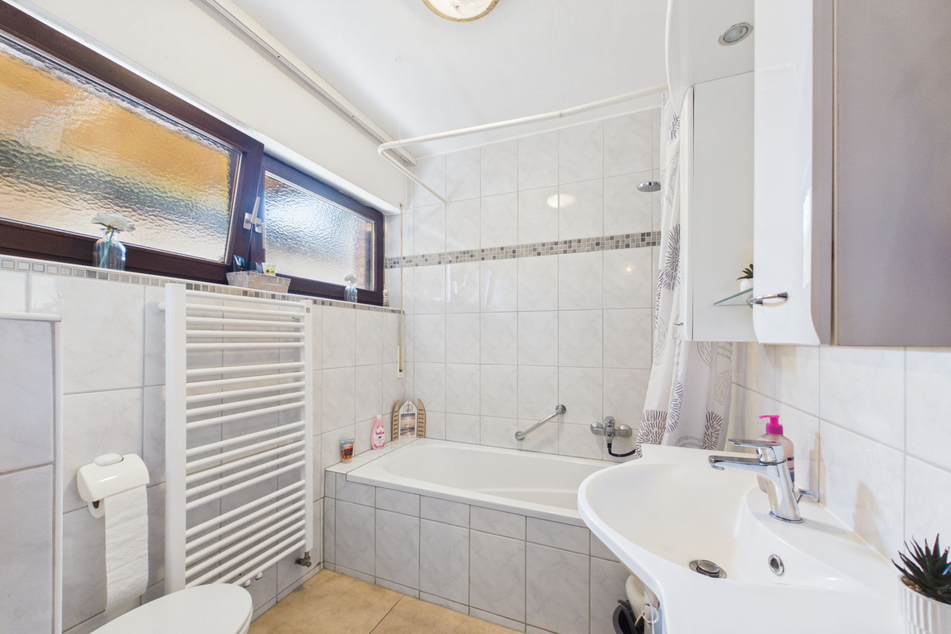 Helles Badezimmer mit Badewanne, Waschbecken, WC, Handtuchheizkörper und Fenster.