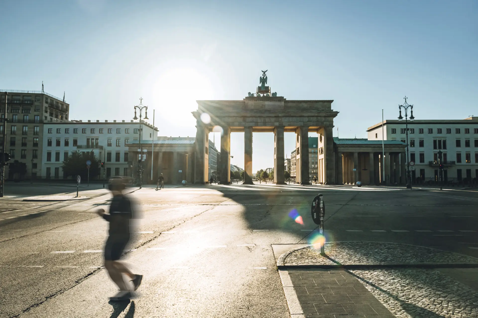 Straße mit großen historischen Torbogen und umgebenden Gebäuden bei Sonnenschein.