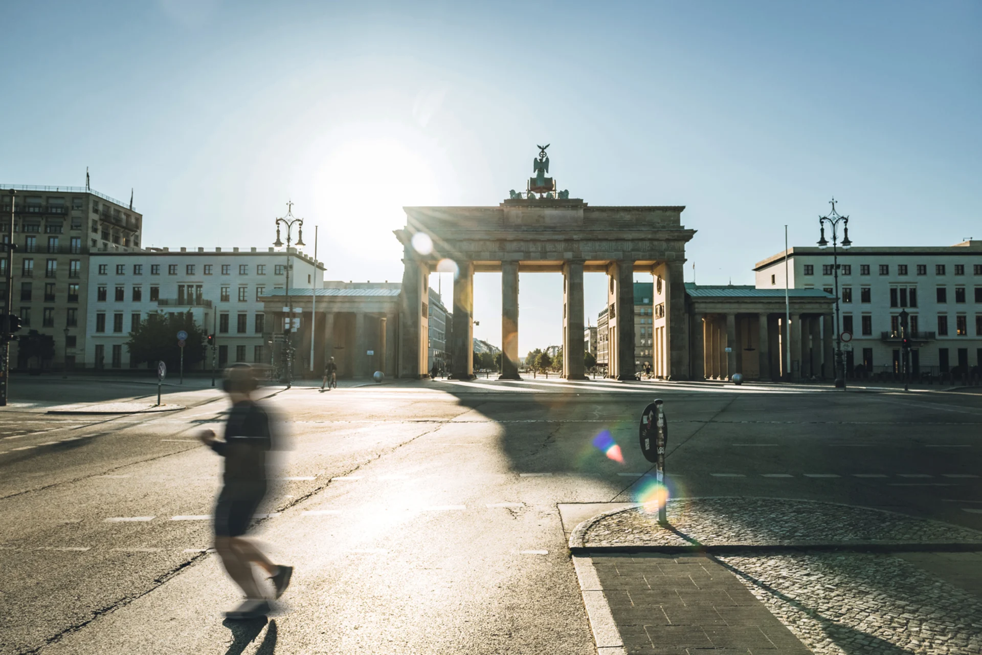 Straße mit großen historischen Torbogen und umgebenden Gebäuden bei Sonnenschein.