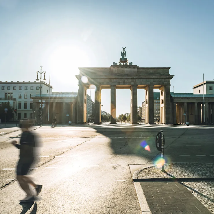 Straße mit großen historischen Torbogen und umgebenden Gebäuden bei Sonnenschein.