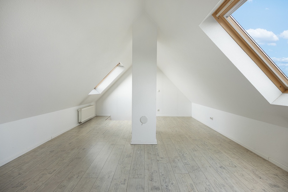 Helles Dachzimmer mit schrägen Wänden, Holzfußboden und zwei Dachfenstern.