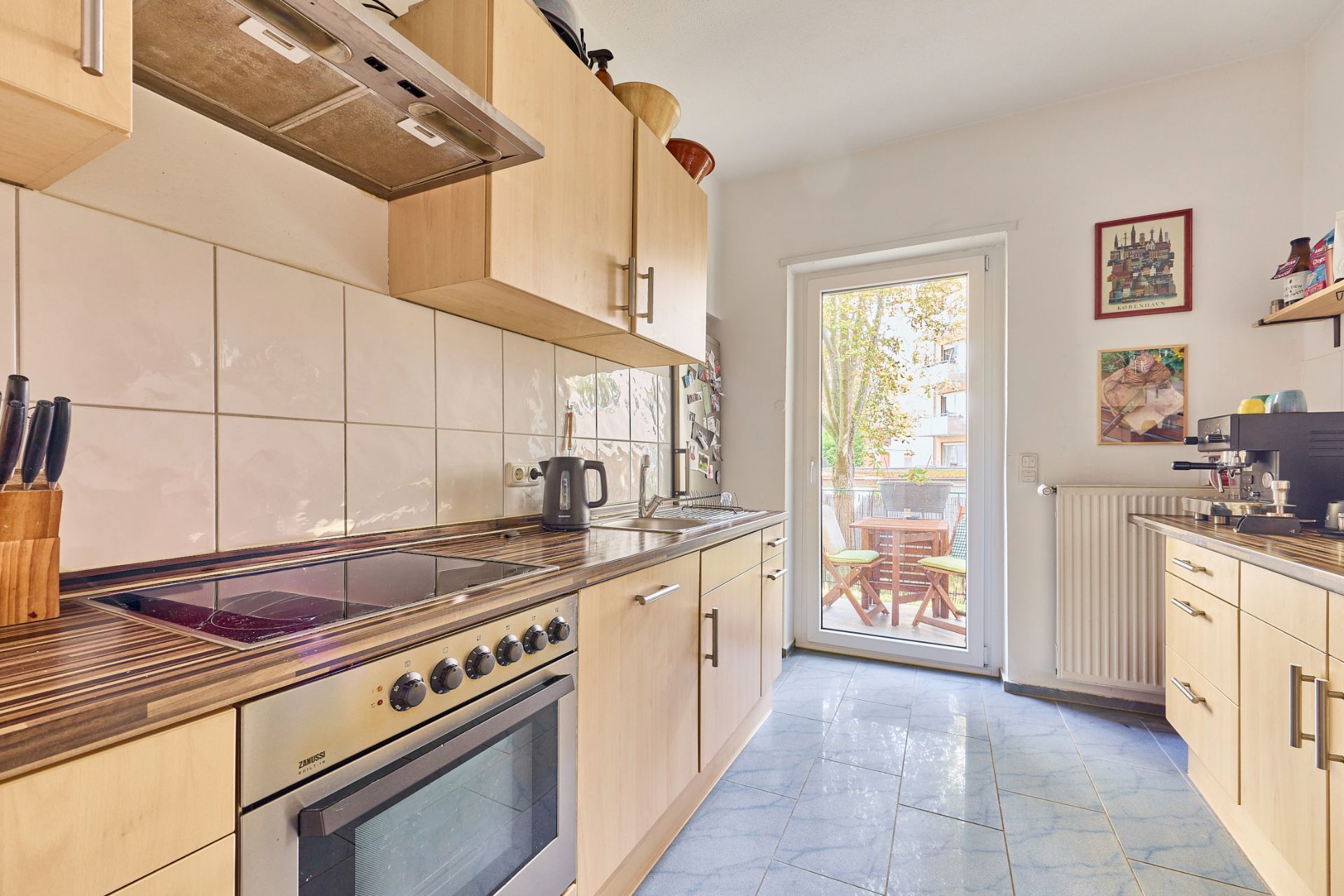 Helle Küche mit Holzmöbeln, Elektroherd und Tür zu einem Balkon mit Tisch und Stühlen.