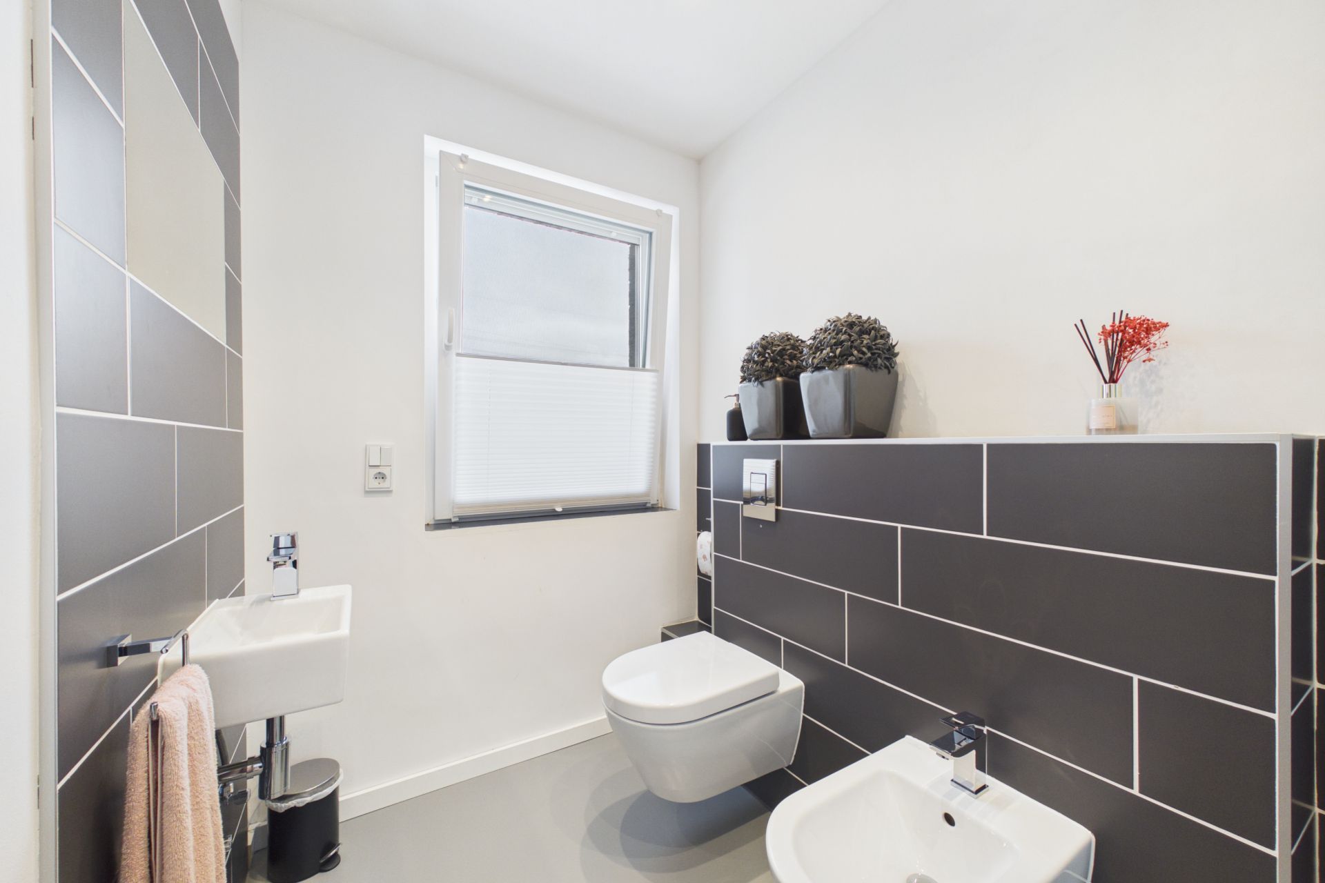 Modernes Badezimmer mit Wand-WC, Bidet, kleinem Waschbecken und Fenster.