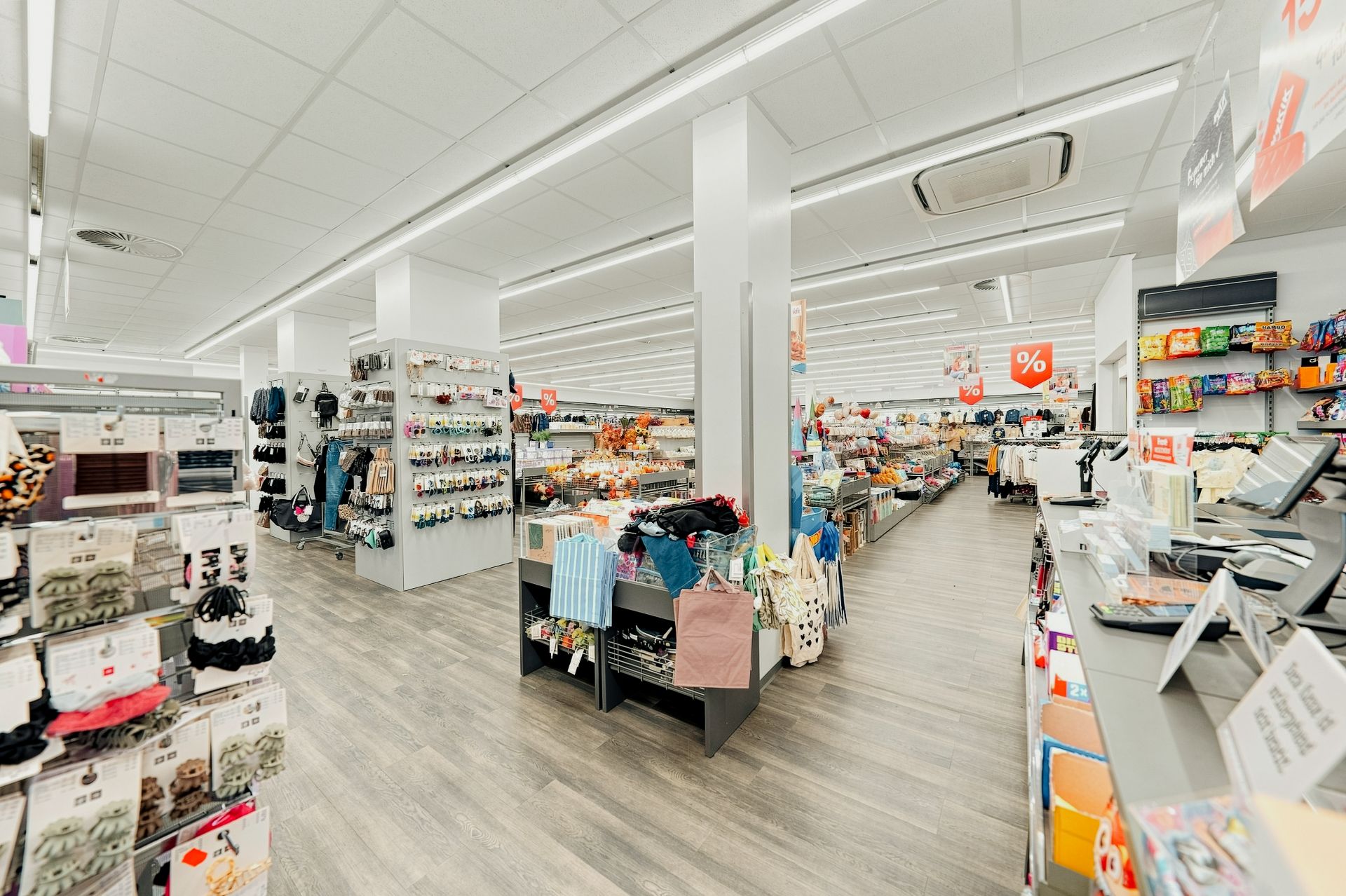 Heller Ladenraum mit Regalen, Kleidung, Accessoires und Kasse im Vordergrund.