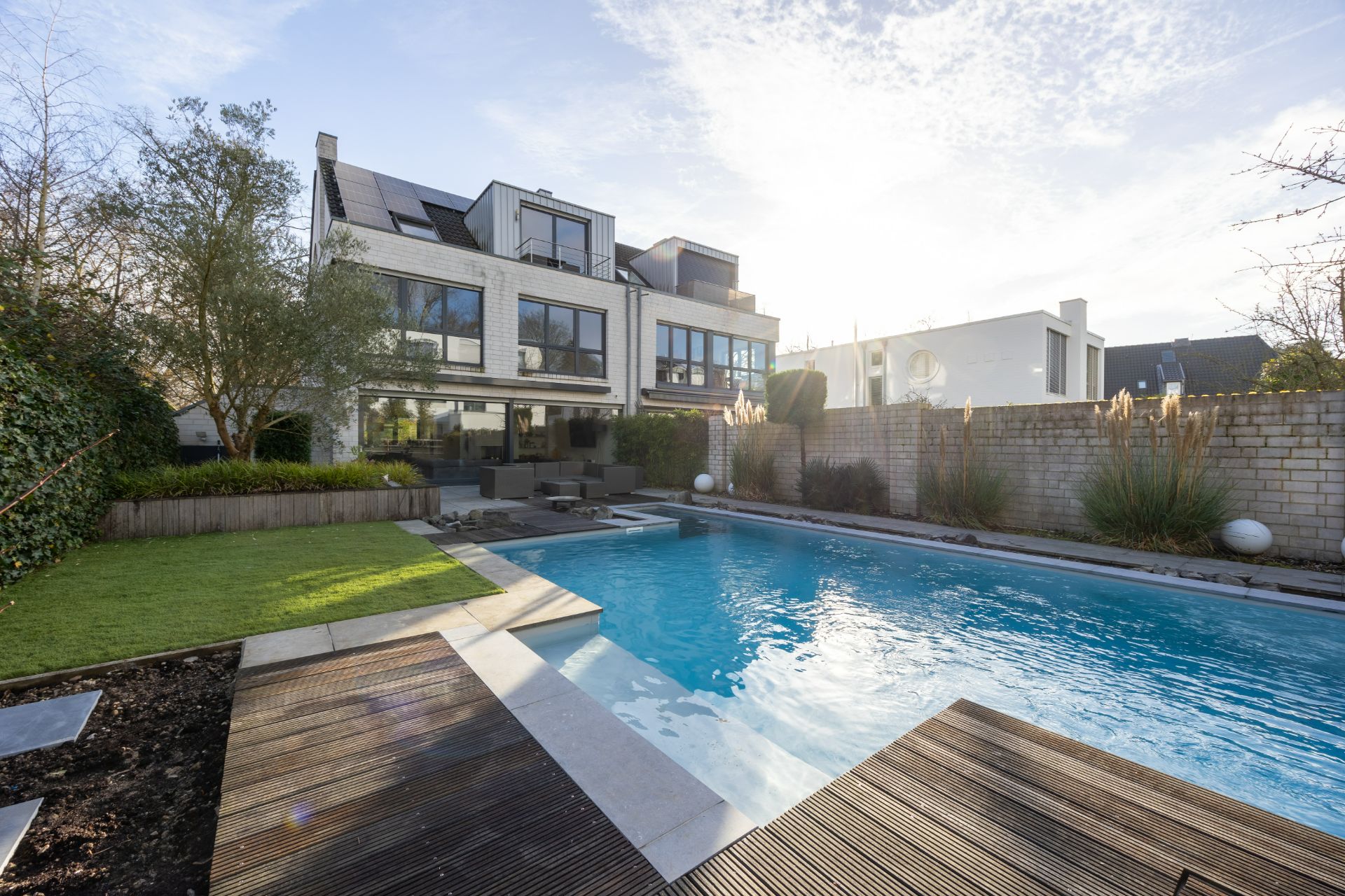 Moderner Garten mit großem Pool, Terrasse, Liegestühlen und Rasenfläche vor einem Wohnhaus.