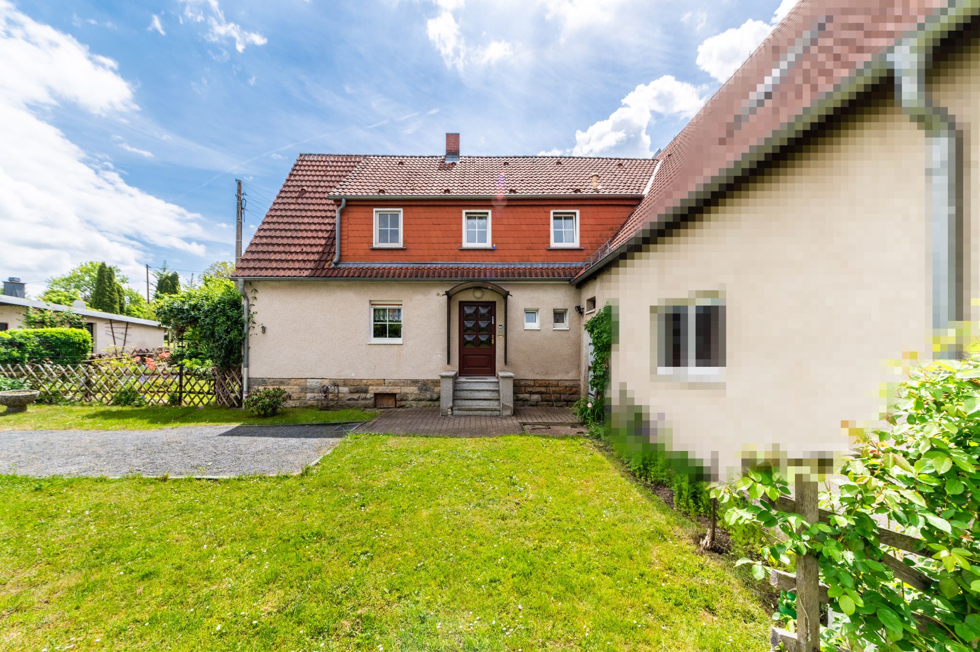 Wohnhaus mit rotem Dach und Vorgarten an einem sonnigen Tag.