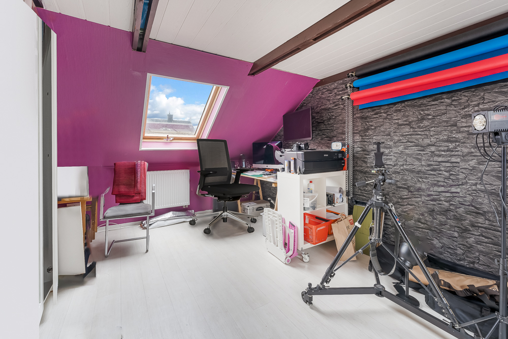 Dachzimmer mit Schreibtisch, Stuhl, Fotostudio-Ausrüstung und farbigen Hintergrundrollen.