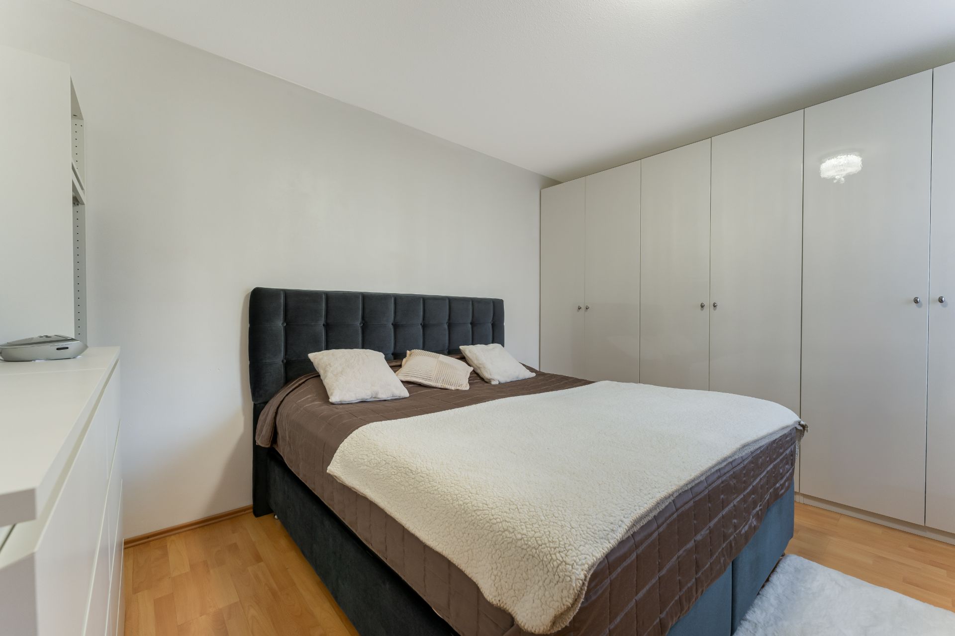 Schlafzimmer mit großem Bett, brauner Bettdecke und weißem Schrank an der Wand.
