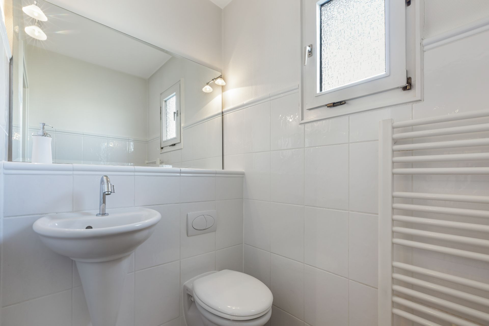 Helles Badezimmer mit Waschbecken, WC, Handtuchheizkörper und Fenster.