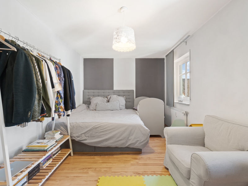 Helles Schlafzimmer mit Bett, Sofa, Kleiderständer und Bücherregal auf Holzfußboden.