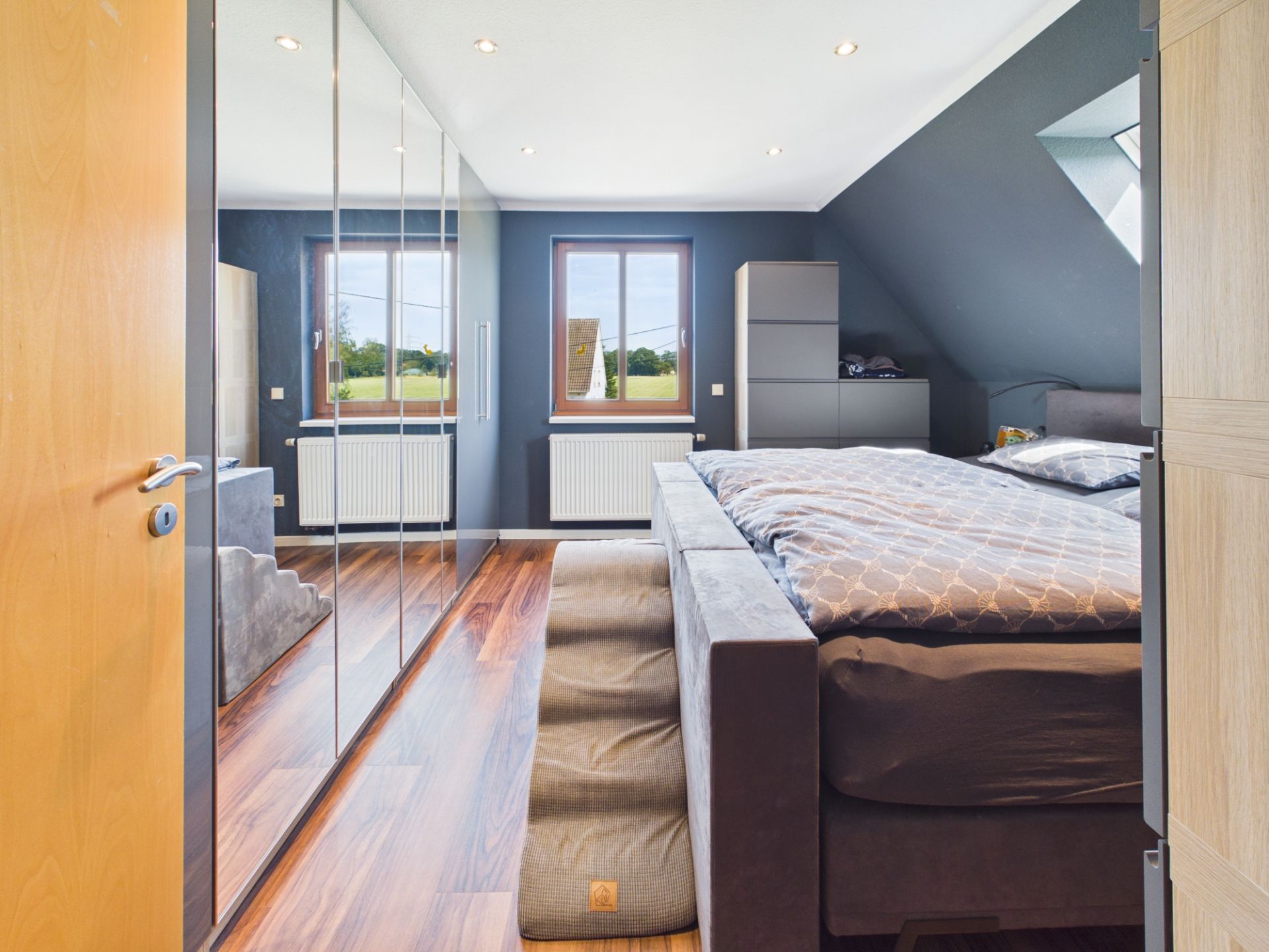 Modernes Schlafzimmer mit Doppelbett, verspiegeltem Kleiderschrank und zwei Fenstern.