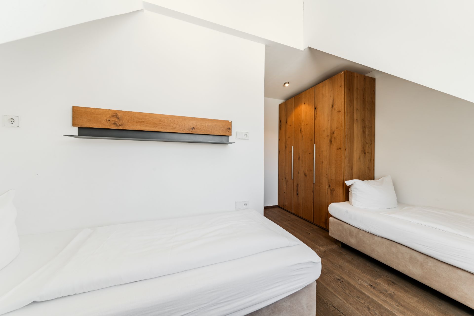 Helles Schlafzimmer mit zwei Einzelbetten, Holzschrank und Wandregal.