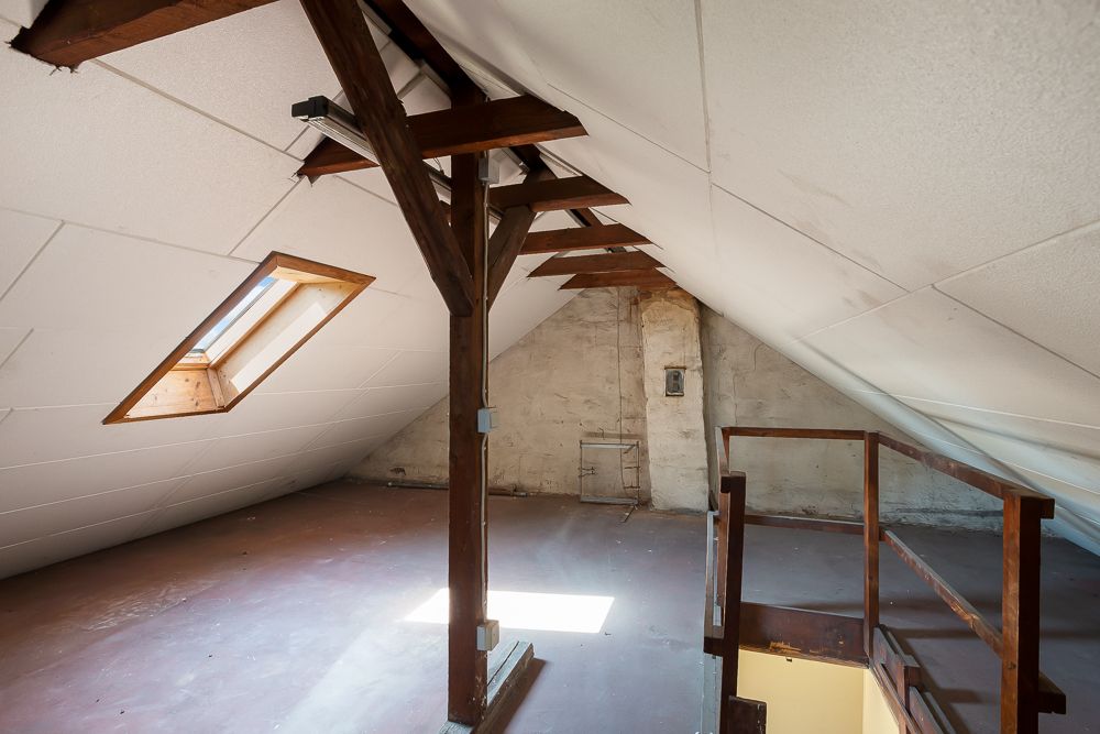 Dachboden mit Holzstützen, Dachfenster und Treppe nach unten.