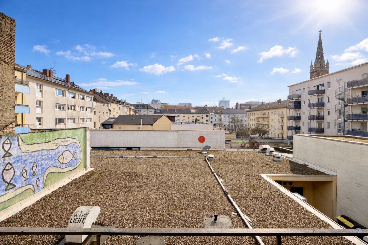 Blick auf Flachdach mit Kies und umliegende Wohngebäude, sonniger Himmel.