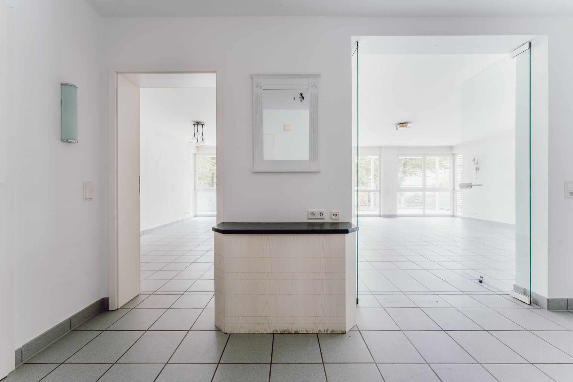 Heller Flur mit Fliesenboden, Spiegel an der Wand und Zugang zu zwei hellen Räumen.