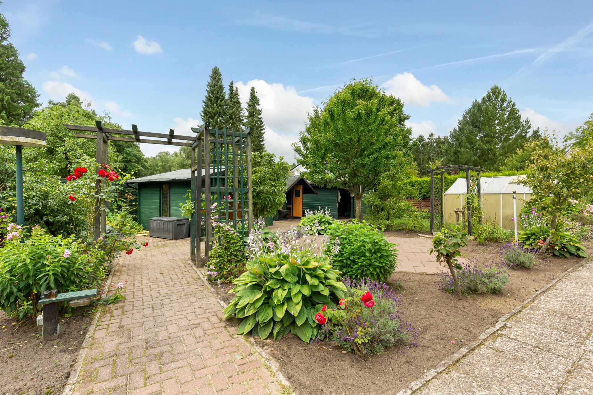 Gepflegter Garten mit Blumen, Wegen, Bänken, kleinem Haus und Gewächshaus.