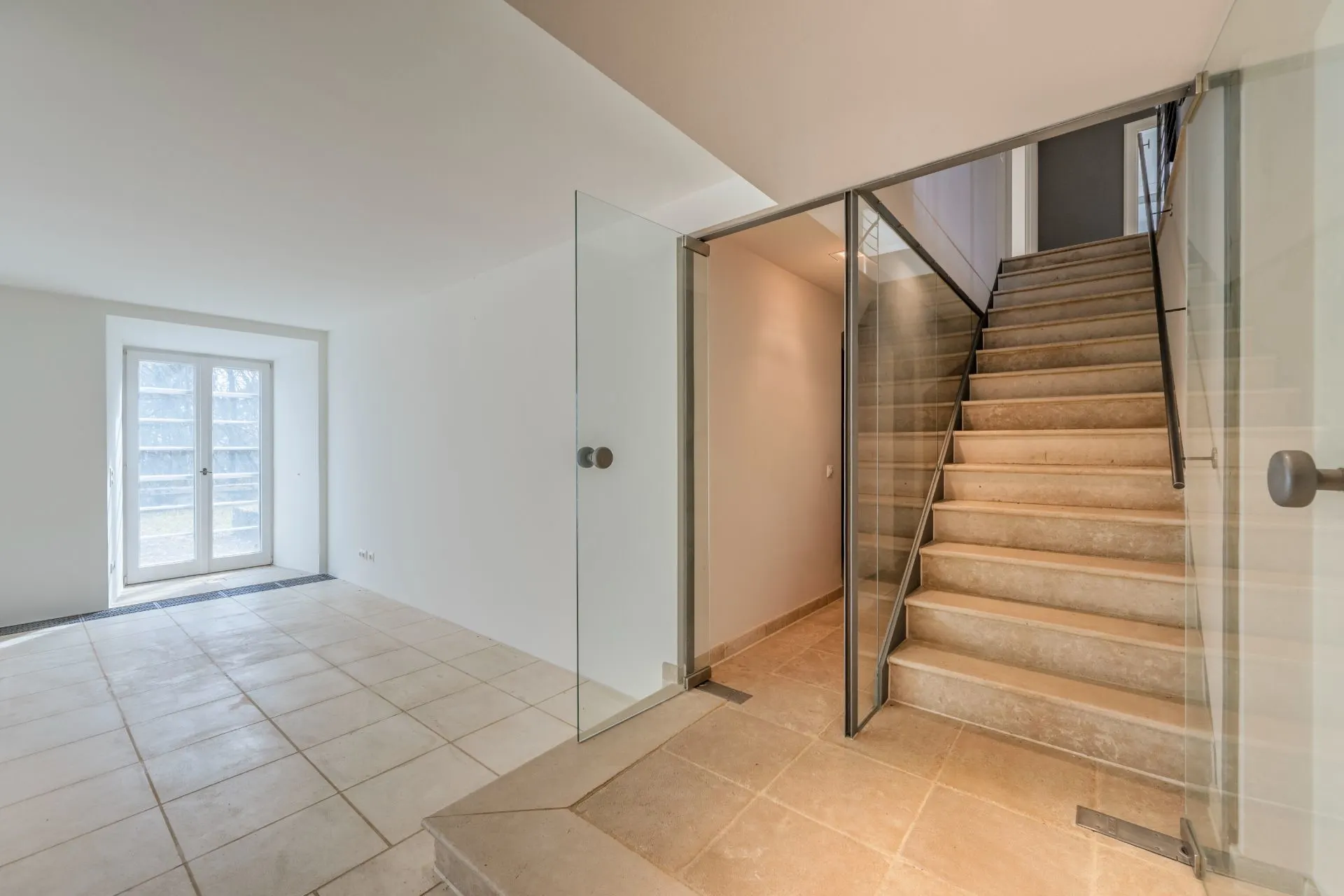 Heller Flur mit Glastüren und Steintreppe, neben einem Raum mit Doppeltür zum Außenbereich.