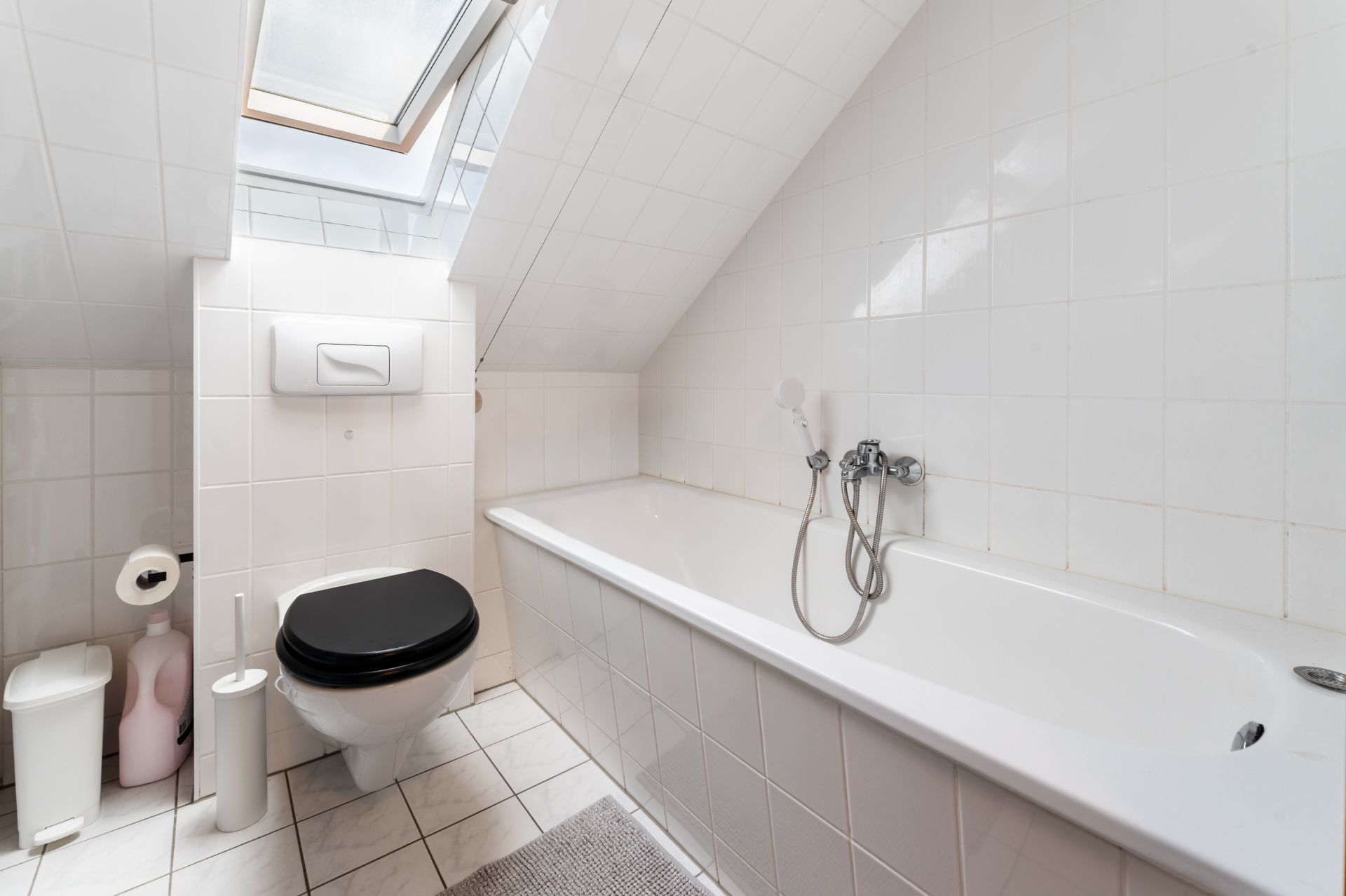 Helles Badezimmer mit Badewanne, Toilette und Dachfenster unter einer Dachschräge.