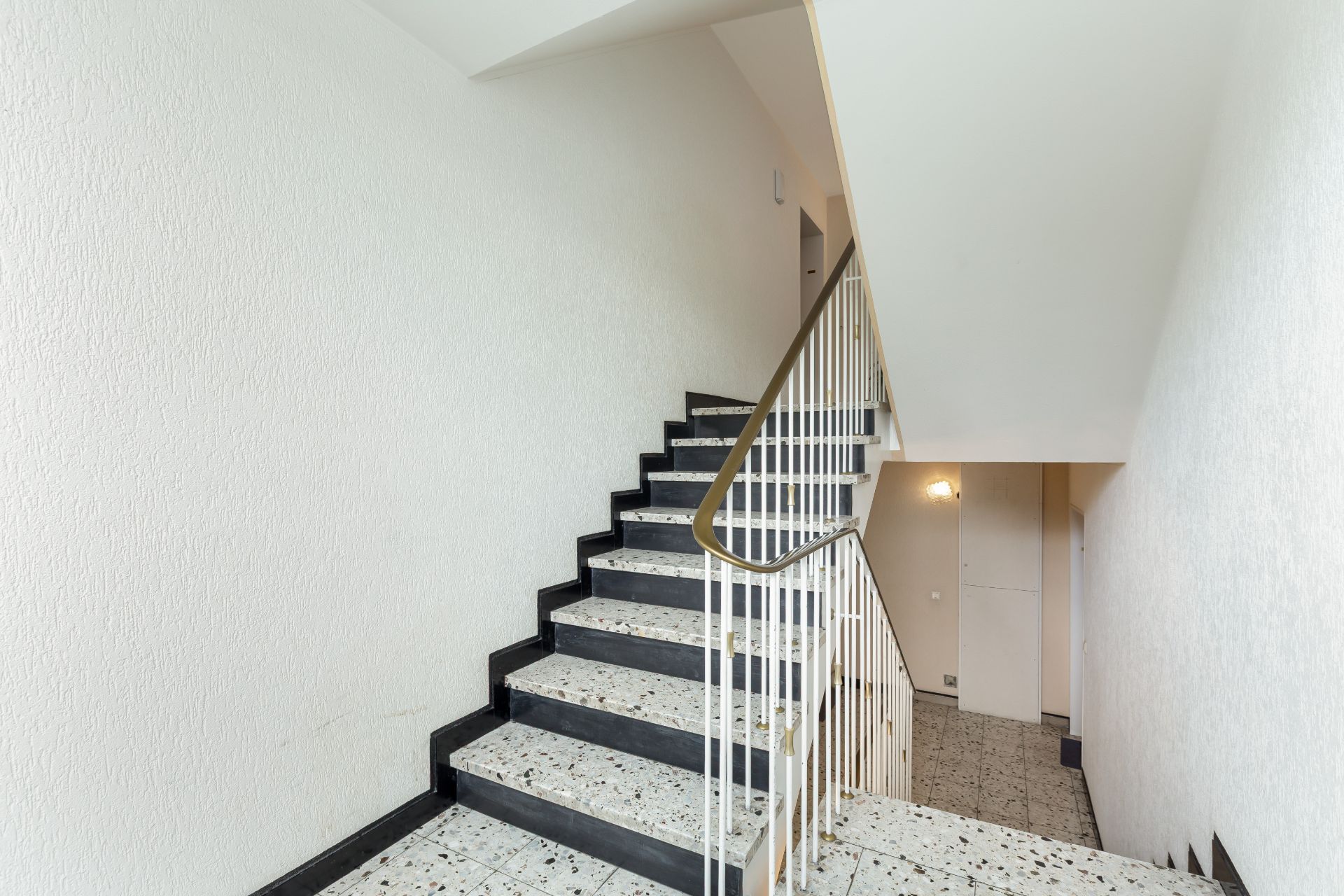 Innen-Treppenhaus mit Marmorstufen und weißem Geländer in einem Wohngebäude.