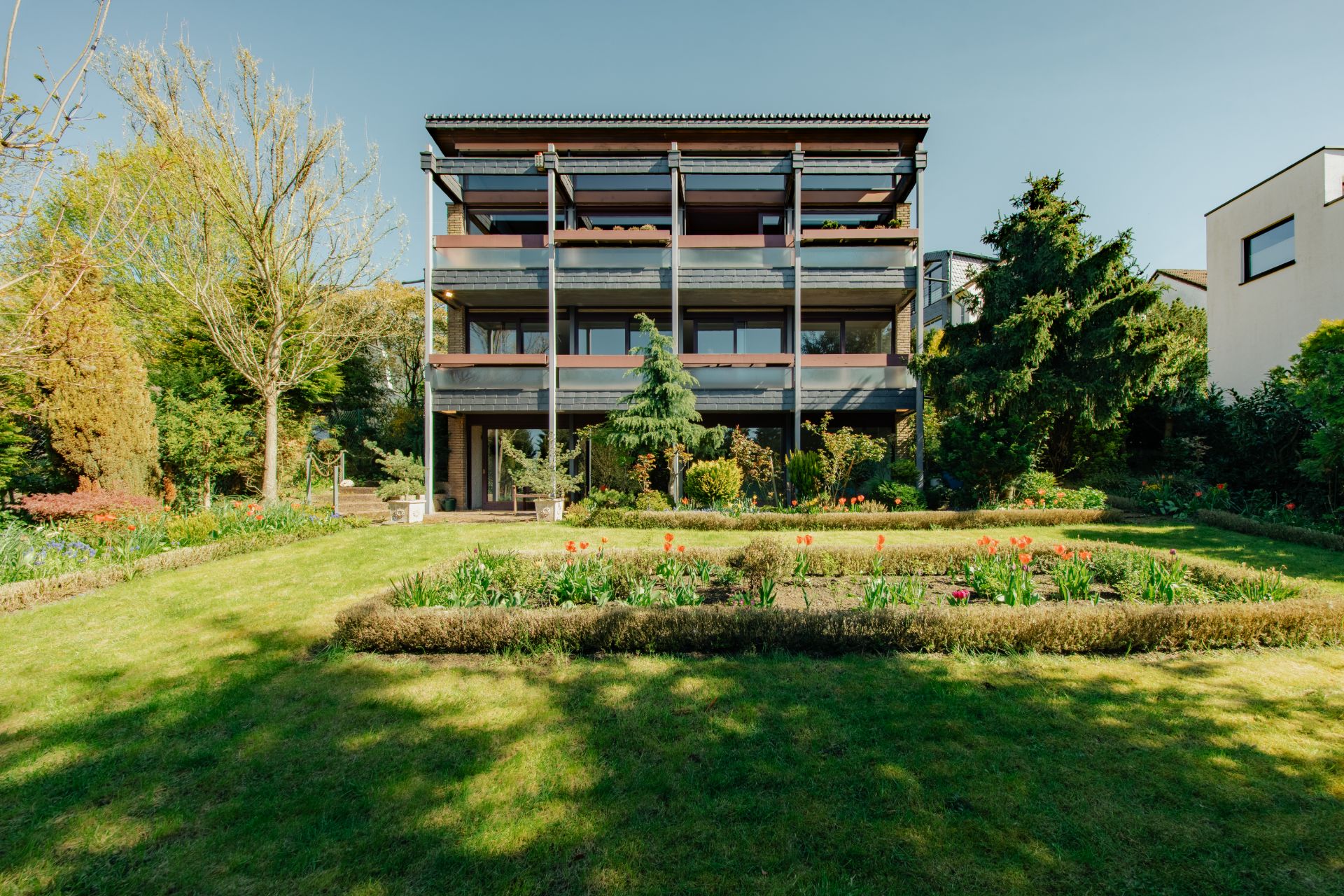 Modernes Wohngebäude mit drei Etagen und großem Garten im Vordergrund.