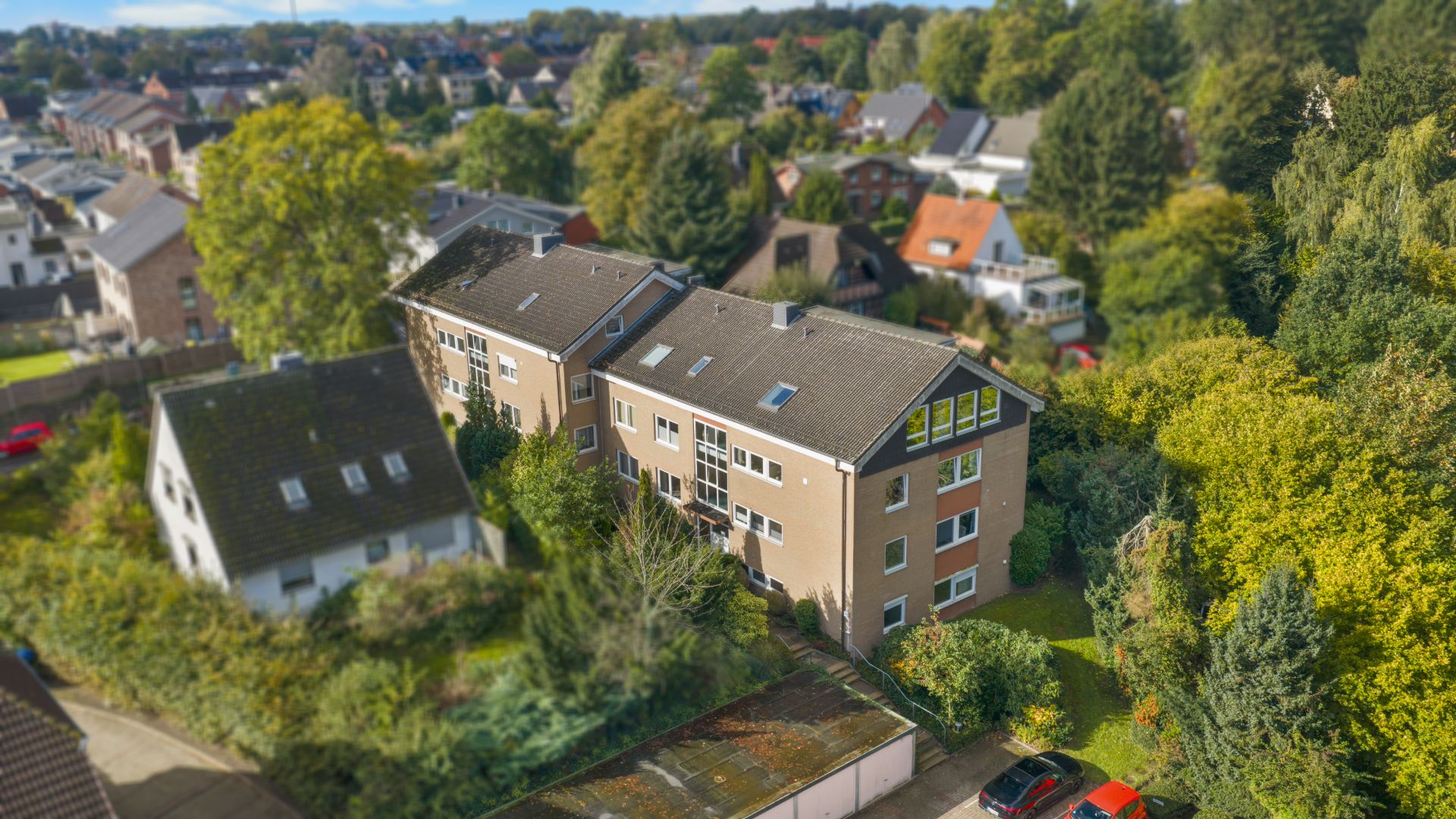 Luftaufnahme eines mehrstöckigen Wohnhauses mit umliegendem Garten und Nachbarhäusern.