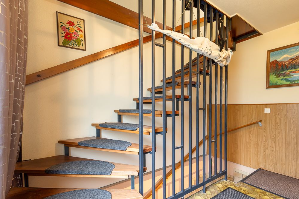 Holztreppe mit schwarzem Geländer, Teppichstufen und bunten Bildern an der Wand.