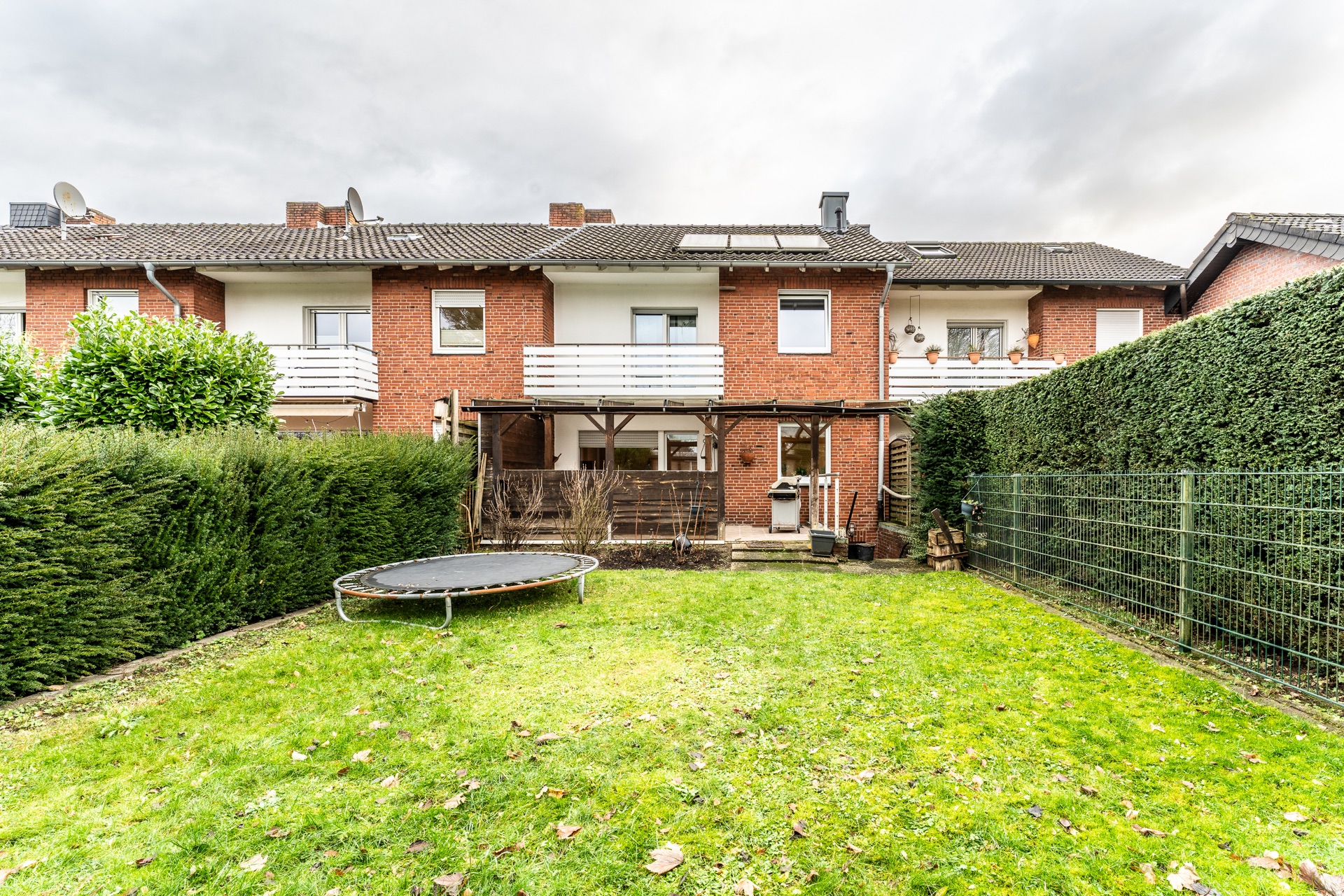 Gepflegter Garten mit Trampolin vor einem Reihenhaus mit Terrasse und Balkon.