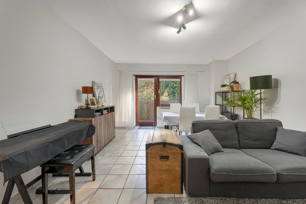 Helles Wohnzimmer mit grauem Sofa, Esstisch, Klavier, Holzkiste und Pflanzen.