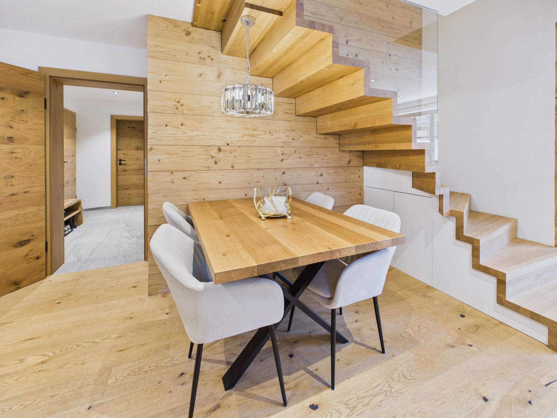 Essbereich mit Holztisch, vier Stühlen und moderner Holztreppe in hellem Raum.
